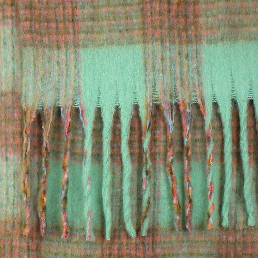 A close-up of a chunky checked scarf in woven wool, featuring a green and brown tartan pattern and fringe with both twisted and untwisted strands at the edge—a perfect accessory for chilly weather.