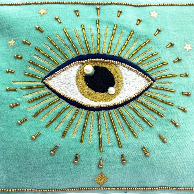 An embroidered eye with gold and pearl details radiates golden lines on teal fabric, surrounded by small stitched stars—an ideal vegan-friendly accessory or unique Christmas present.
