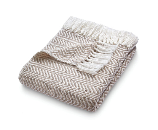 The eco-friendly Herringbone Throw, crafted from recycled plastic bottles, boasts a folded beige and white herringbone pattern with fringed edges on a pristine white background.