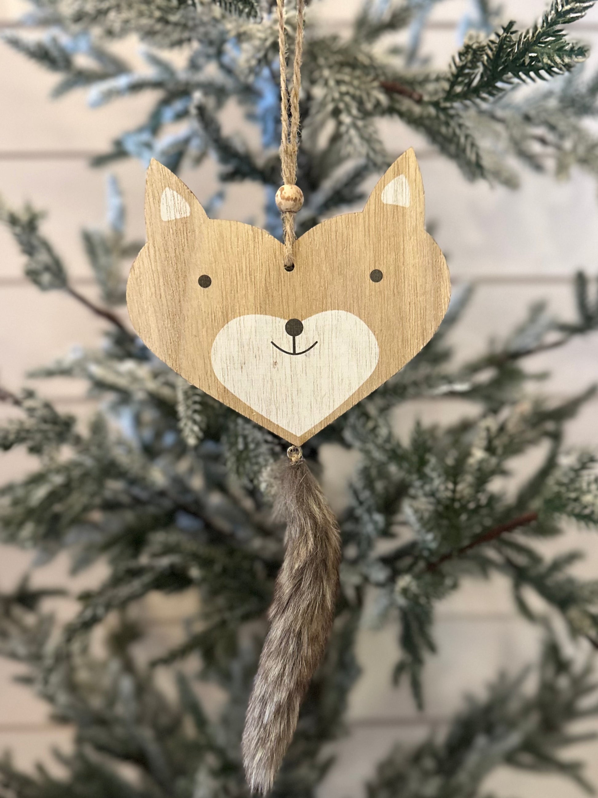Wooden fox Christmas decoration with painted details and a faux fur tail, hanging from a branch of an artificial, snow-dusted Christmas tree—a delightful addition to your woodland Christmas décor.