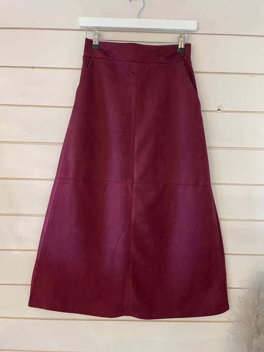 A vegan-friendly, maroon A-line skirt is displayed on a white hanger against a light wooden wall.