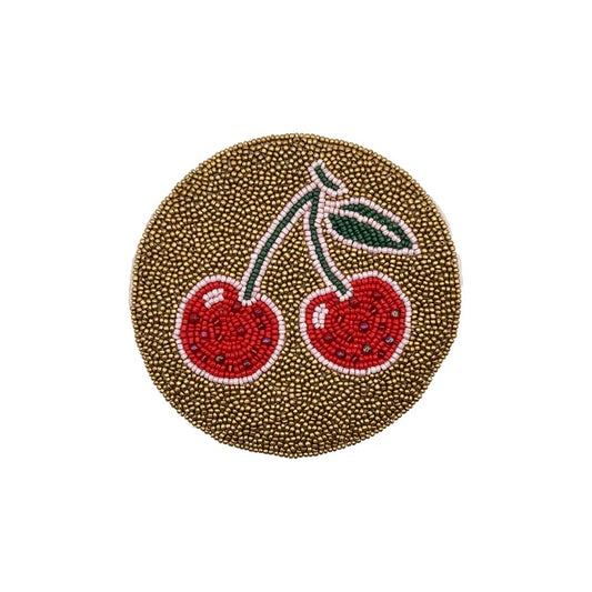 A round coaster adorned with small gold beads and a beaded motif of two red cherries with green leaves—ideal as a festive Christmas gift or a delightful vegan accessory for your home.