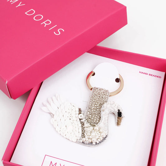 A hand-crafted swan-shaped keyring adorned with glass beads rests in a pink box labelled MY DORIS.