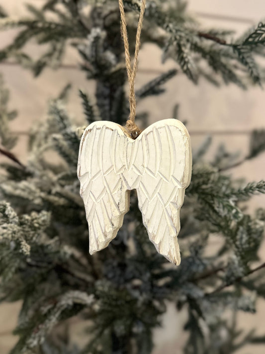 A white wooden angel wings ornament hangs from twine on a Christmas tree with green, frosted branches, bringing a charming touch to your festive décor.