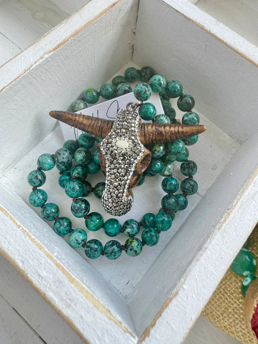 A green beaded bracelet featuring a decorative buffalo head pendant sits in a white wooden display box.