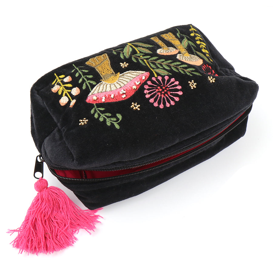 A black velvet bag adorned with colourful, embroidered floral patterns and toadstools, featuring a pink tassel on the zip—a charming choice for makeup storage.