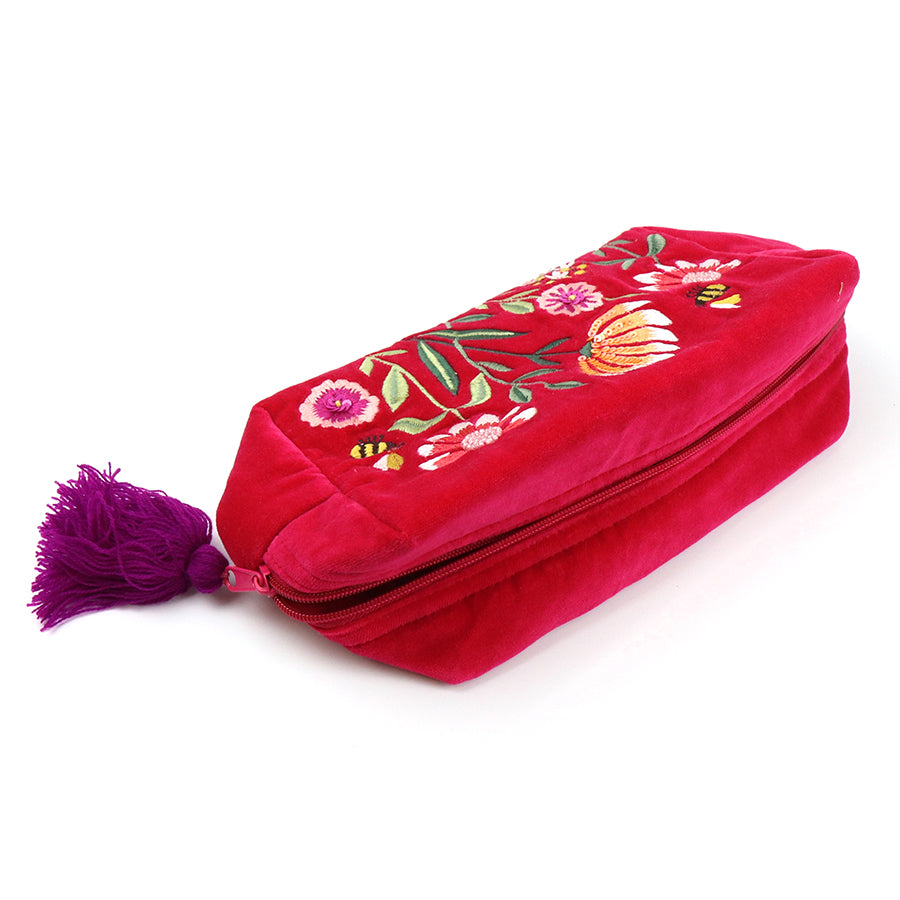 A chic make-up bag crafted from fuchsia velvet, featuring exquisite floral embroidery and a purple tassel on the zip.