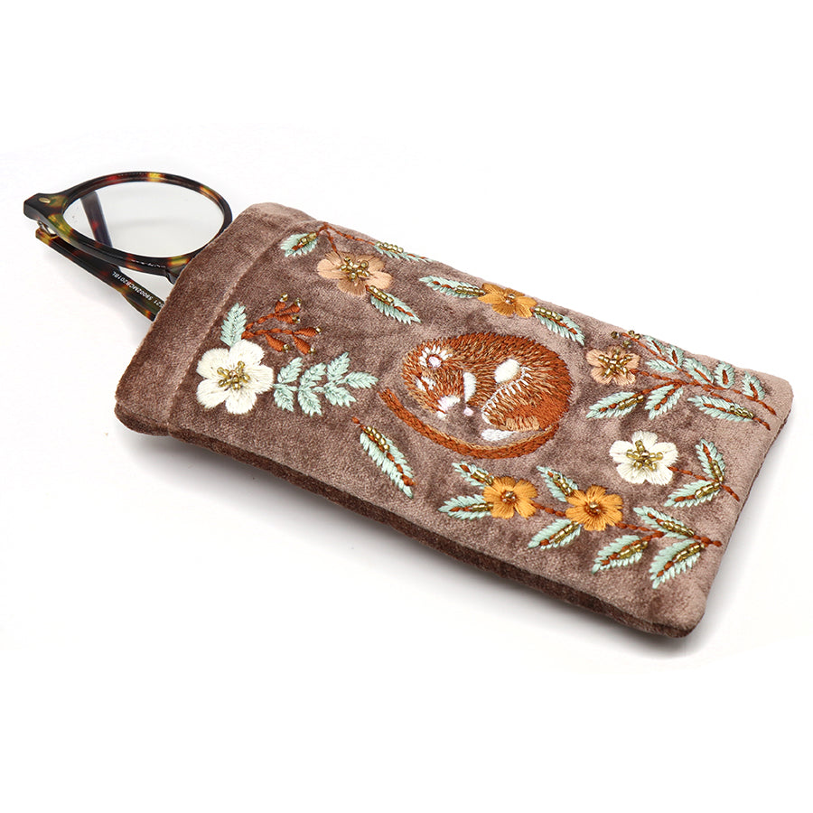 A pair of spectacles partly tucked into a taupe velvet glasses case, providing stylish protection for eyewear with embroidered flowers and a heart.