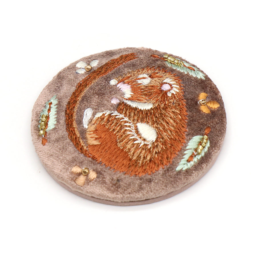 A round brown fabric patch decorates this embroidered compact mirror, displaying a curled-up mouse encircled by delicate leaves and tiny beads.