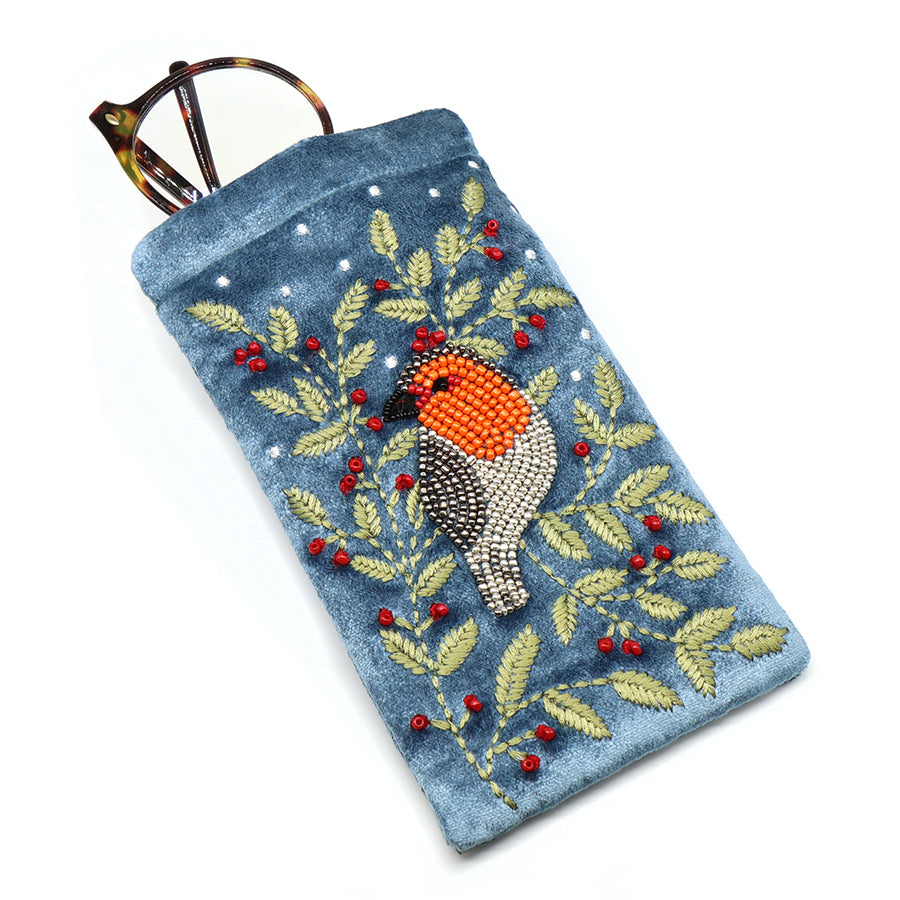 A blue velvet glasses case featuring an embroidered robin, red berries, and green leaves, with a pair of tortoiseshell spectacles partially tucked inside.