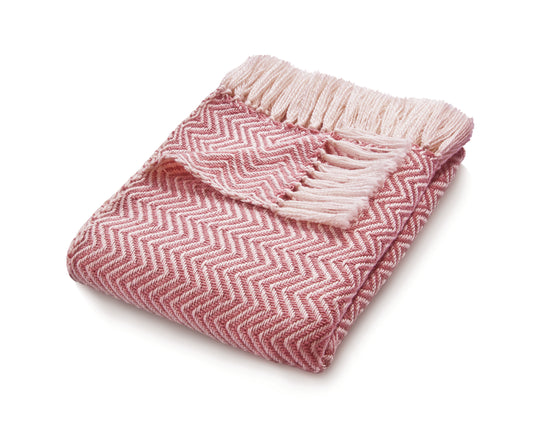 An eco-friendly pink and white herringbone throw, crafted from recycled plastic bottles, features fringe ends and lies against a pristine white background.