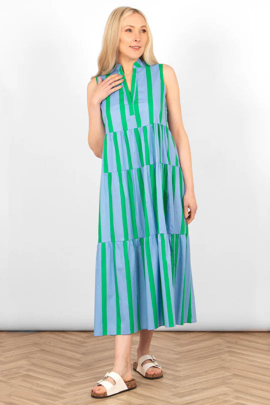 A woman with long blonde hair is wearing an Ainsley Tiered Maxi Dress featuring blue and green block stripes, standing on a wood-patterned floor against a white background.