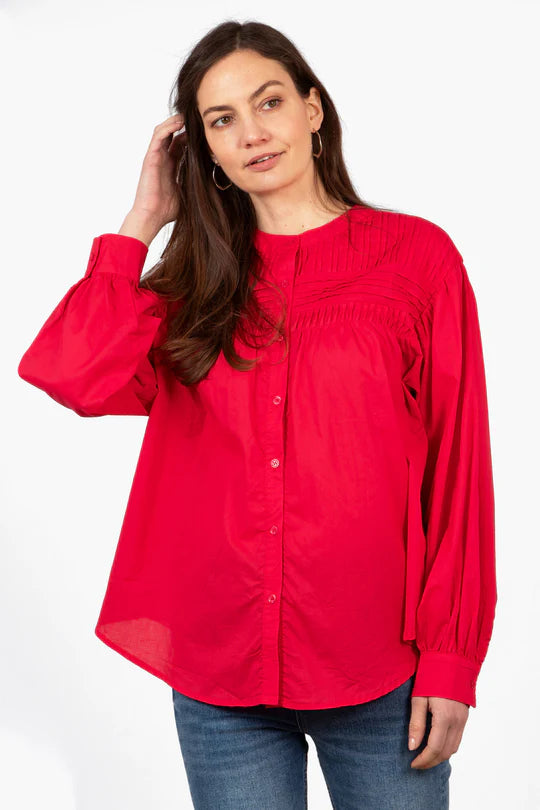 A person with long hair wearing an elegant Libby Long Sleeve Red Button-Down Shirt and blue jeans, standing against a plain white background.