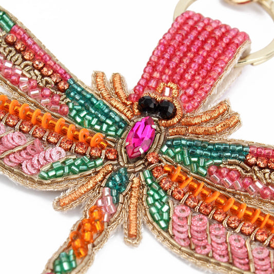 The Pink Dragonfly Keyring exhibits exquisite beadwork with vibrant patterns in pink, orange, green, and gold beads, all centred around a striking pink gem. Perfect for adding a touch of artistry to your belongings.