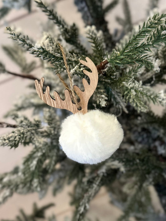 A Christmas tree branch adorned with a white fluffy Deer Pom Pom ornament, complete with wooden antlers and resembling a reindeer, brings a charming touch to your festive décor.