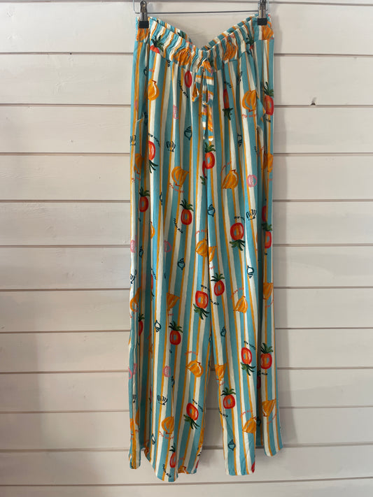 Wide-leg, lightweight trousers with blue and white stripes and playful fruit prints, made from vegan-friendly fabric—ideal for casual wear, shown against a white wooden wall.