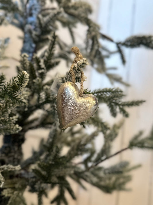 A vegan-friendly, eco-friendly Heart Christmas Tree Decoration hangs from a twine loop on a snow-dusted evergreen branch against a light background.
