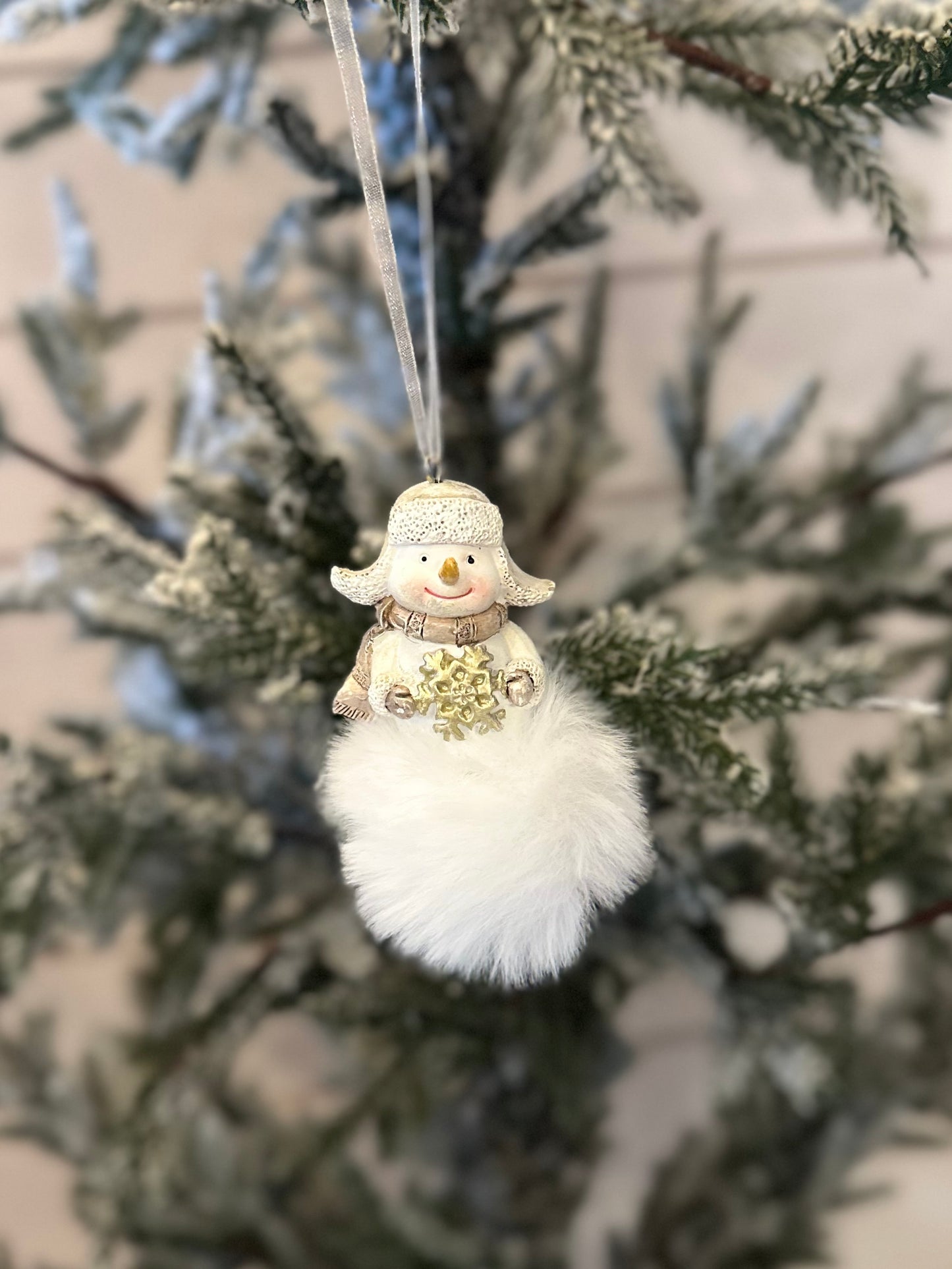 A handmade ornament, this snowman decoration with a white fluffy base hangs from a Christmas tree branch with frosted needles.