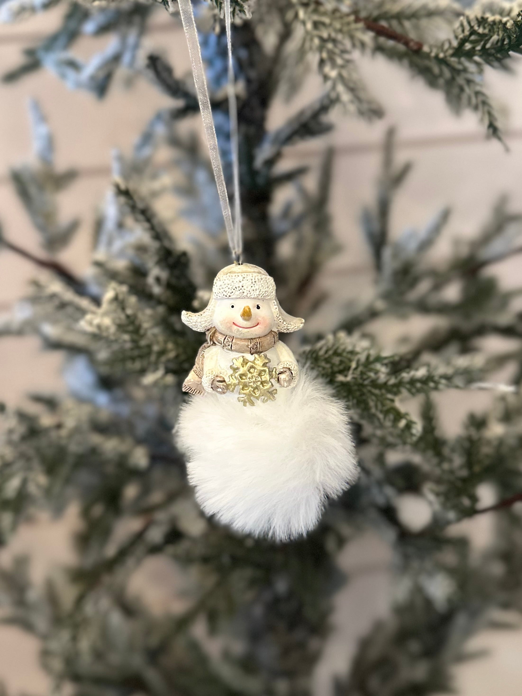 A handmade ornament, this snowman decoration with a white fluffy base hangs from a Christmas tree branch with frosted needles.