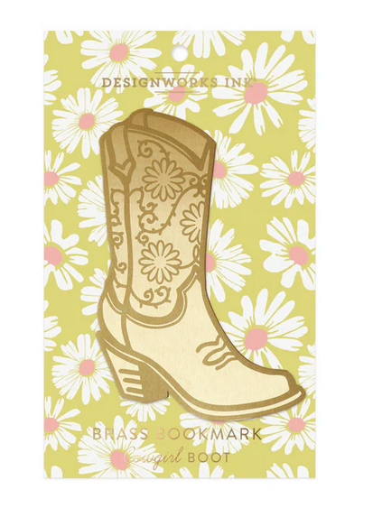 A Western-inspired brass bookmark shaped like a cowgirl boot is presented on a yellow card decorated with white daisy patterns.