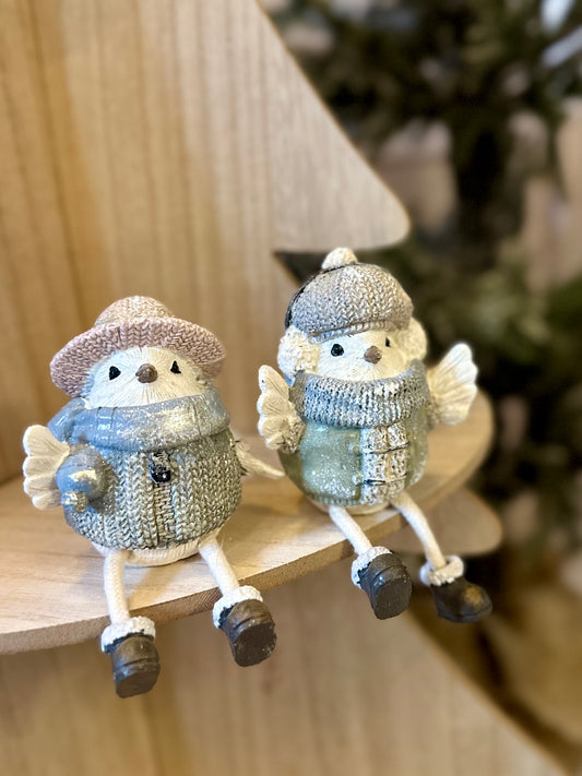 Two decorative bird ornaments, one a delightful female bird in a pink hat, sit side by side in festive jumpers and scarves on a wooden shelf, ideal for Christmas décor.