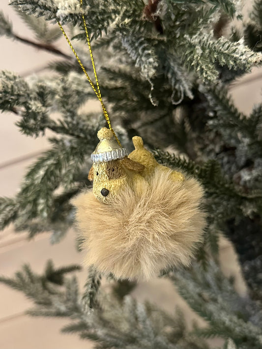 A delightful Doggy Christmas Tree Decoration showcasing a gold-coloured bear with a silver hat, clutching a fluffy tan pom-pom, hanging from a snow-dusted tree branch—perfect for festive décor and dog lovers.