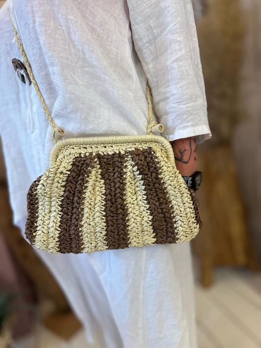Person wearing a white outfit carries a small, rectangular, brown and beige striped straw bag with a gold chain strap for an environmentally-friendly touch. Rewritten in British English: A person dressed in white carries a small, rectangular straw bag with brown and beige stripes and a gold chain strap, adding an environmentally friendly touch.