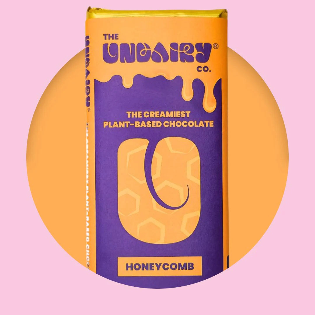 A purple and yellow UnDairy chocolate bar labelled The UnDairy Co. Honeycomb, The Creamiest Plant-Based Chocolate, rests on a pink and orange background—an ethically conscious treat you’ll love.
