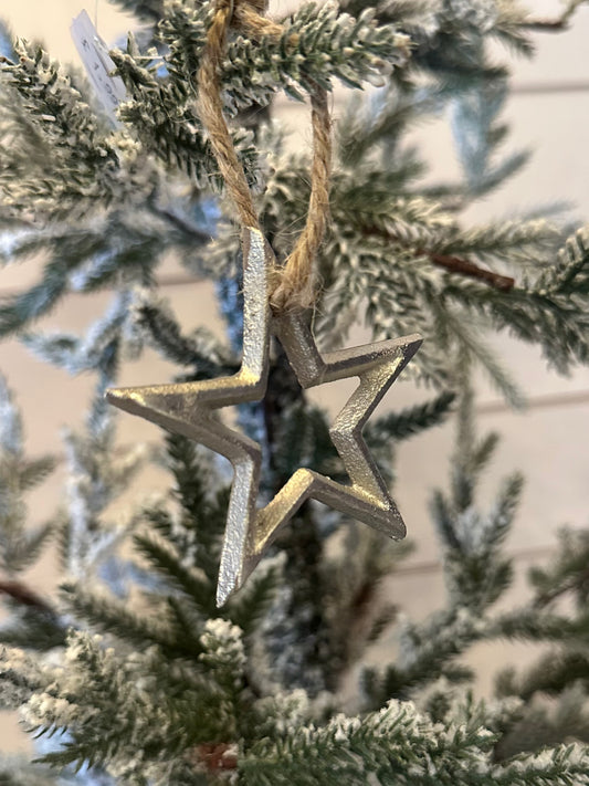 A silver Christmas star tree decoration hangs from a twine loop on a snow-dusted artificial tree, ideal for those looking for environmentally friendly Christmas décor.