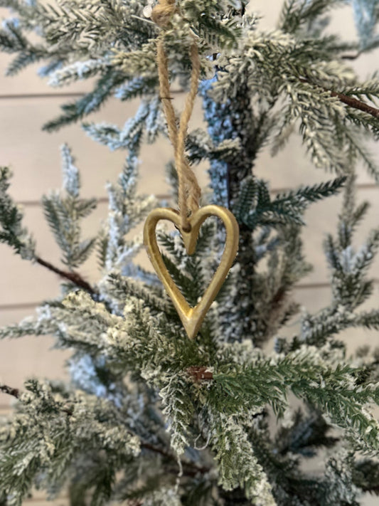 A gold, vegan-friendly Christmas heart tree decoration hangs by a twine string on a snow-dusted artificial evergreen, adding festive charm to your holiday décor.