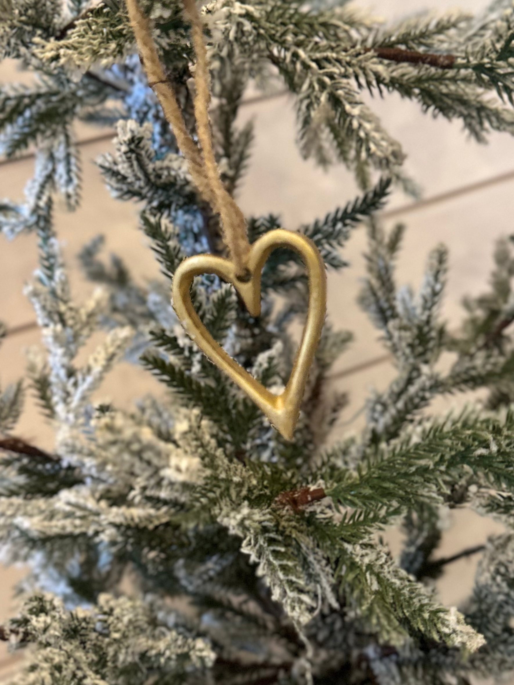 A gold, heart-shaped ornament, an ideal Christmas Heart Tree Decoration, hangs on a snow-dusted artificial pine branch—delightful vegan-friendly festive décor.