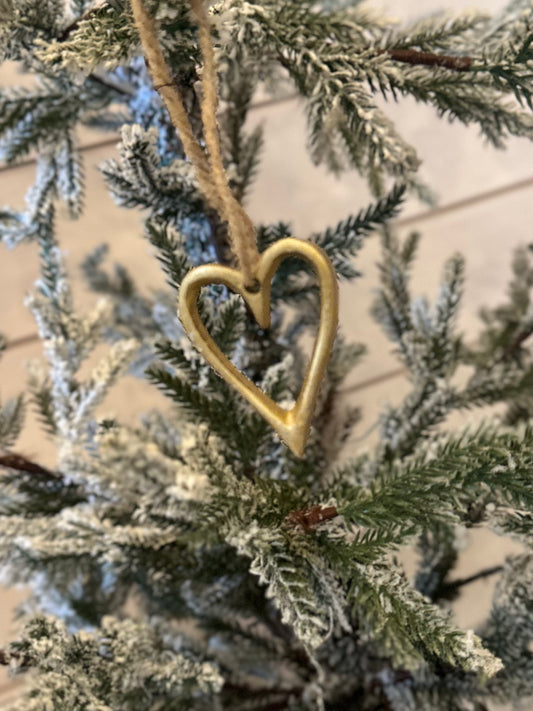 A gold, heart-shaped ornament, an ideal Christmas Heart Tree Decoration, hangs on a snow-dusted artificial pine branch—delightful vegan-friendly festive décor.