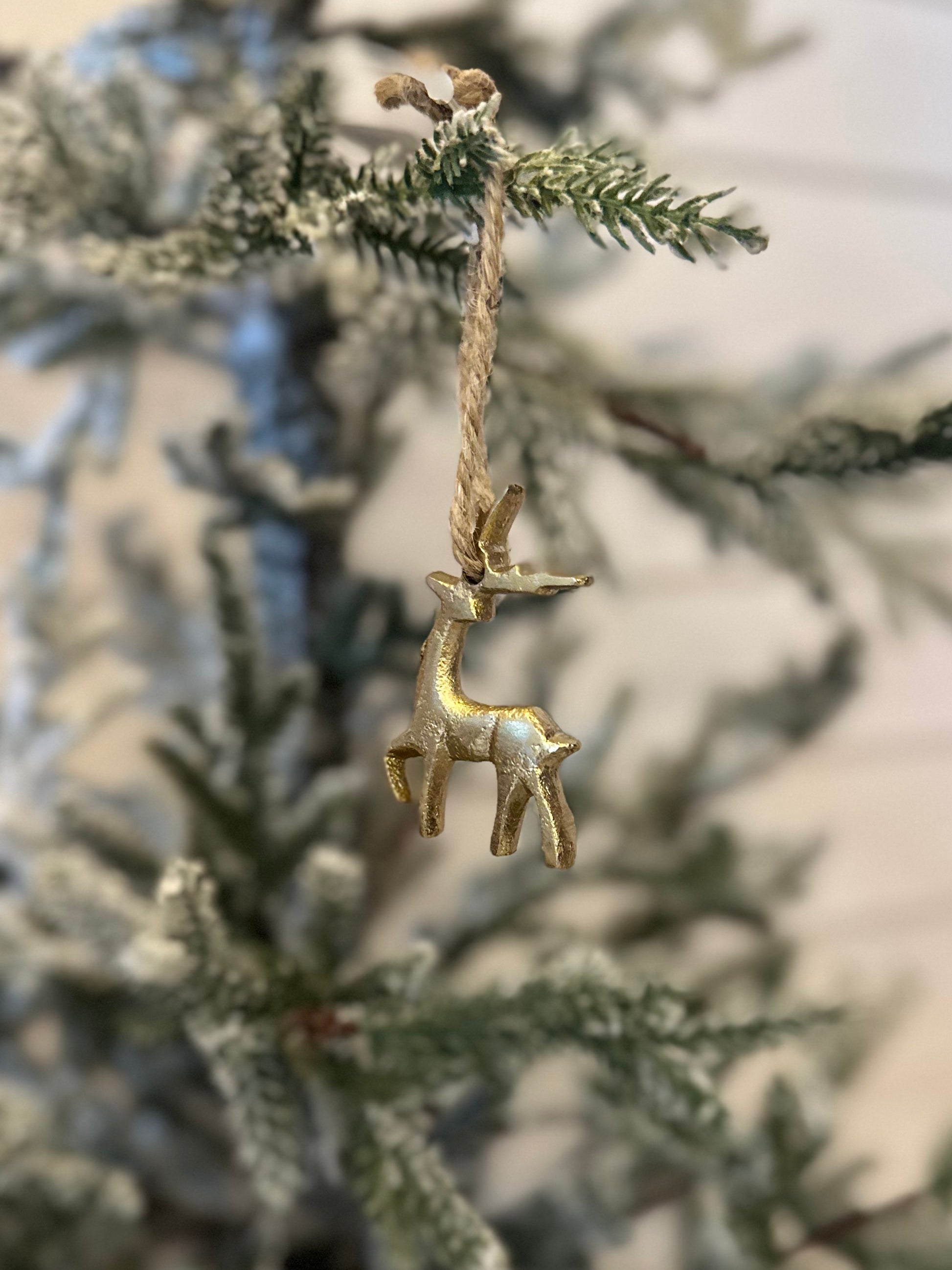A gold hanging reindeer ornament dangles from a twine string on a frosted artificial pine branch, adding a festive touch to your Christmas decor.