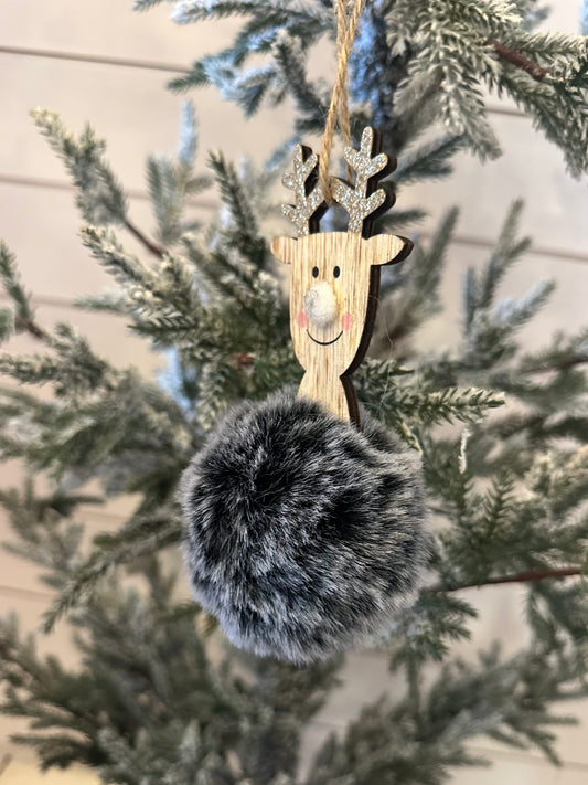A charming deer decoration with glittery antlers and a large, fluffy, grey pom-pom body hangs on a snow-dusted artificial Christmas tree, adding festive holiday décor to your space.