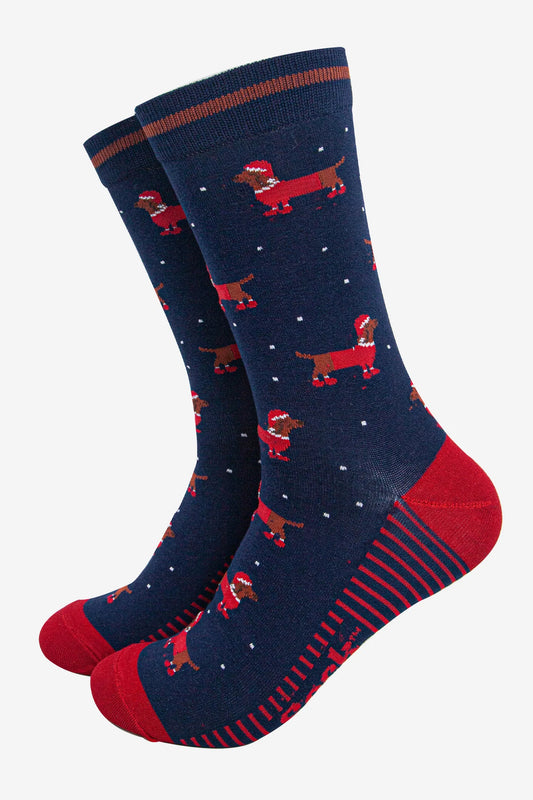Pair of navy blue socks with red heels and toes, adorned with a pattern of dachshunds wearing Santa hats and scattered white dots—ideal Christmas socks and a delightful dachshund gift for the festive season.