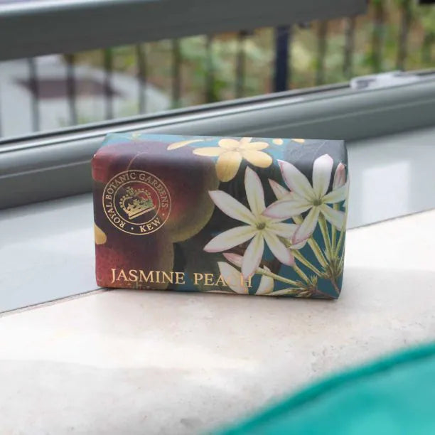 A bar of Kew Gardens Jasmine Peach Soap, wrapped in floral packaging and labelled vegan soap, rests on a windowsill—an eco-friendly gift for any occasion.