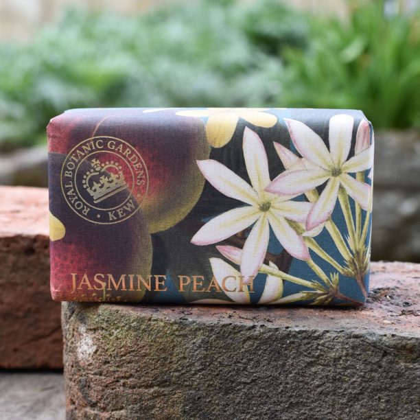A bar of Kew Gardens Jasmine Peach Soap, a vegan soap wrapped in floral-patterned paper, rests on a stone surface outdoors—an eco-friendly present ideal for any occasion.