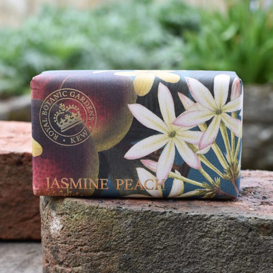A bar of Kew Gardens Jasmine Peach Soap, a vegan soap wrapped in floral-patterned paper, rests on a stone surface outdoors—an eco-friendly present ideal for any occasion.