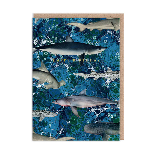 The Marble Sharks Greeting Card features a dynamic design of various sharks swimming against a blue oceanic background, with the words Happy Birthday elegantly displayed in the centre.