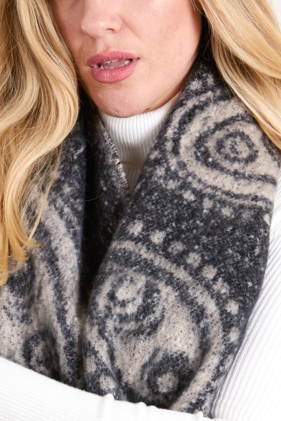 A woman dressed in a white polo-neck jumper and a thick, vegan black paisley scarf.