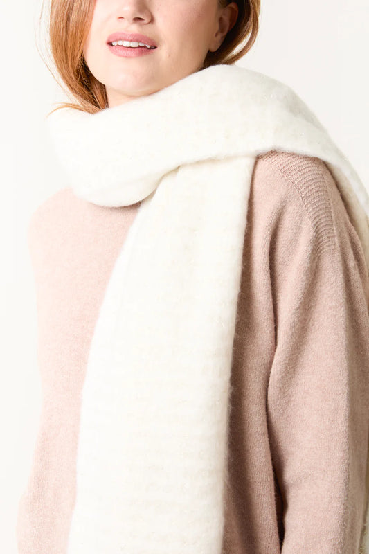 A woman wearing a light pink jumper and a thick, white, cruelty-free scarf draped around her neck.