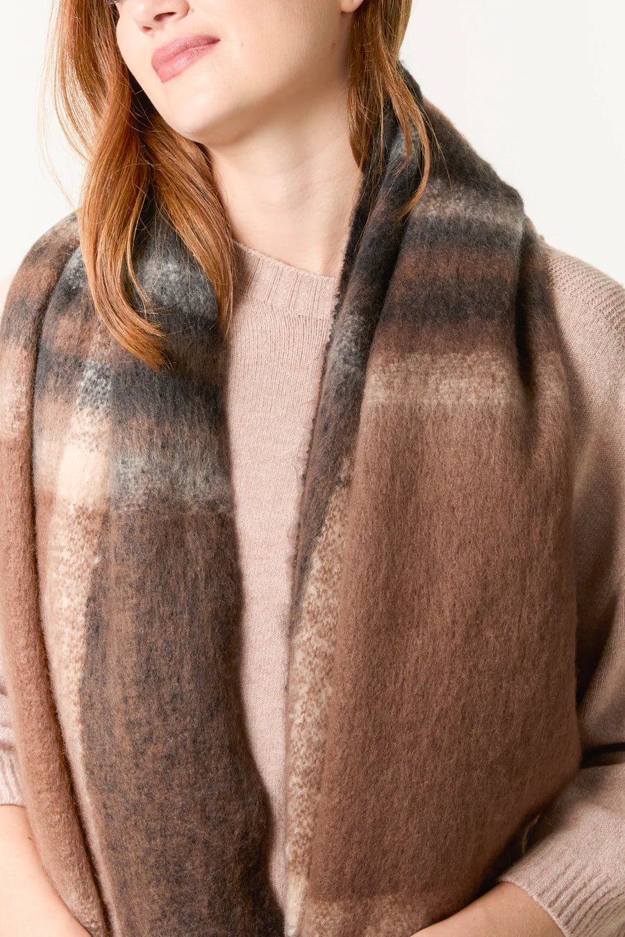 A woman wearing a soft brown and grey checked scarf over a light pink jumper, facing slightly to the side.