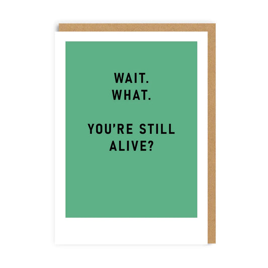 Cheeky A6 greeting card featuring a green front with black text that reads, Wait. What. Youre still alive? Perfect as a humourous birthday card for those with a playful spirit!.