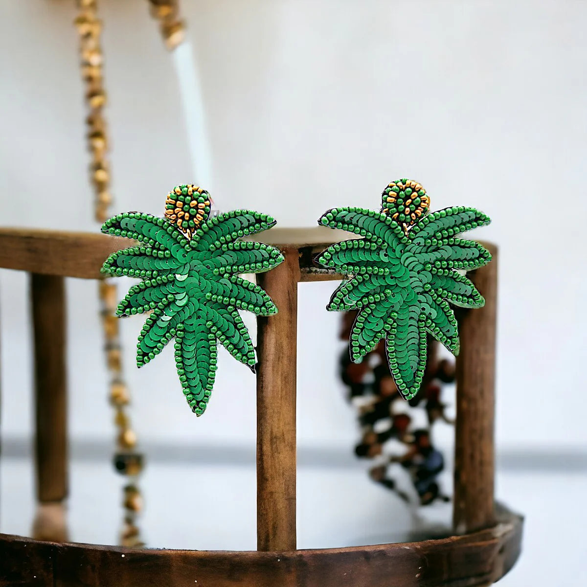 A pair of palm leaf earrings shaped like green leaves with intricate patterns, displayed on a wooden stand.