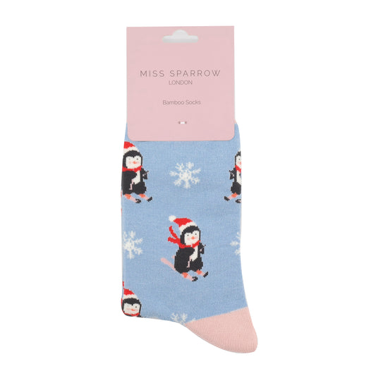 Light blue Christmas Skiing Penguin Socks crafted from bamboo, showcasing skiing penguins in red hats among white snowflakes—an ideal vegan present, presented with a pink Miss Sparrow London label.