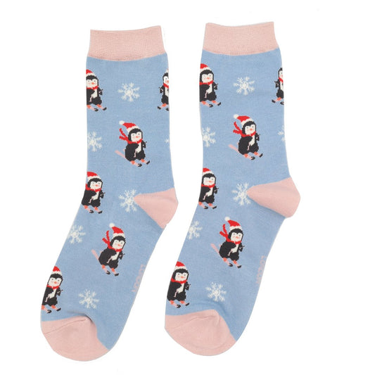 Light blue bamboo socks with pink toes and cuffs, featuring skiing penguins in Santa hats and red scarves for Christmas, along with white snowflakes—a perfect vegan gift for the festive season.