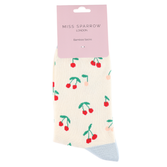 A pair of cream-coloured Mini Cherries Cream Socks featuring a cherry pattern, pale blue toe, and a pink “Miss Sparrow London Bamboo Socks” label—crafted from vegan-friendly bamboo and cotton.