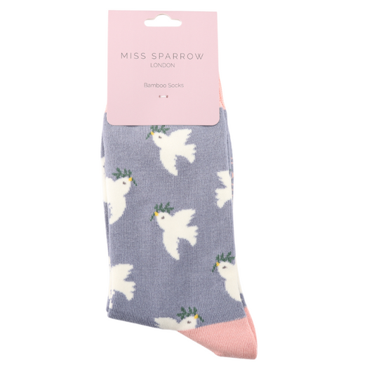 A pair of Doves Denim Socks made from soft bamboo and cotton, featuring white doves and green wreaths, fits UK sizes 3–7, packaged with a pink Miss Sparrow London label.