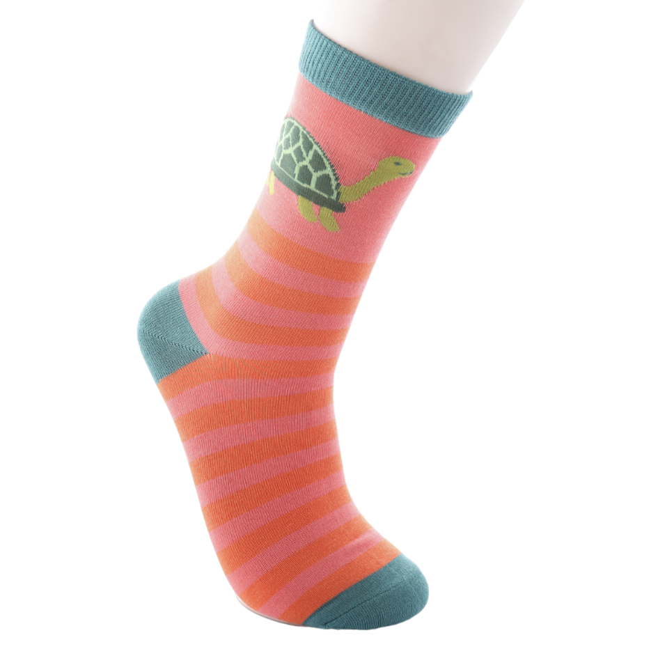 A foot wearing a pink and orange striped sock with teal accents and a green turtle motif, crafted from a soft bamboo and cotton blend.