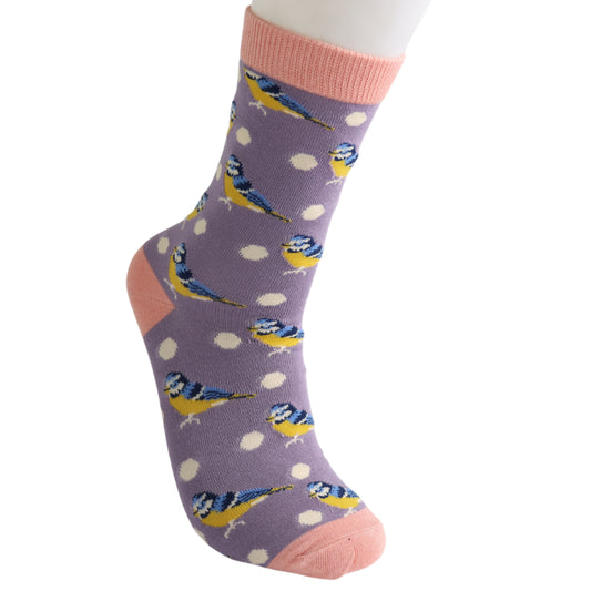 A British design, these Bluetits & Spots Lilac bamboo socks feature white polka dots, blue and yellow bird illustrations, and pink accents on the toe, heel, and cuff.